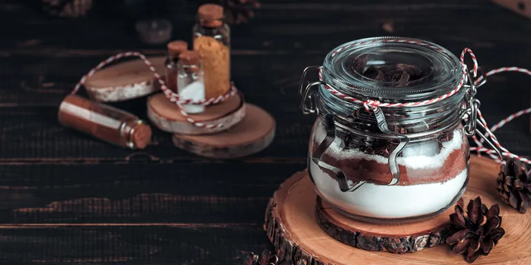 Geschenk aus der Küche Backmischung geschichtet in einem Weckglas auf mehreren rustikalen Holzscheiben stehend mit Tannenzapfen dekoriert